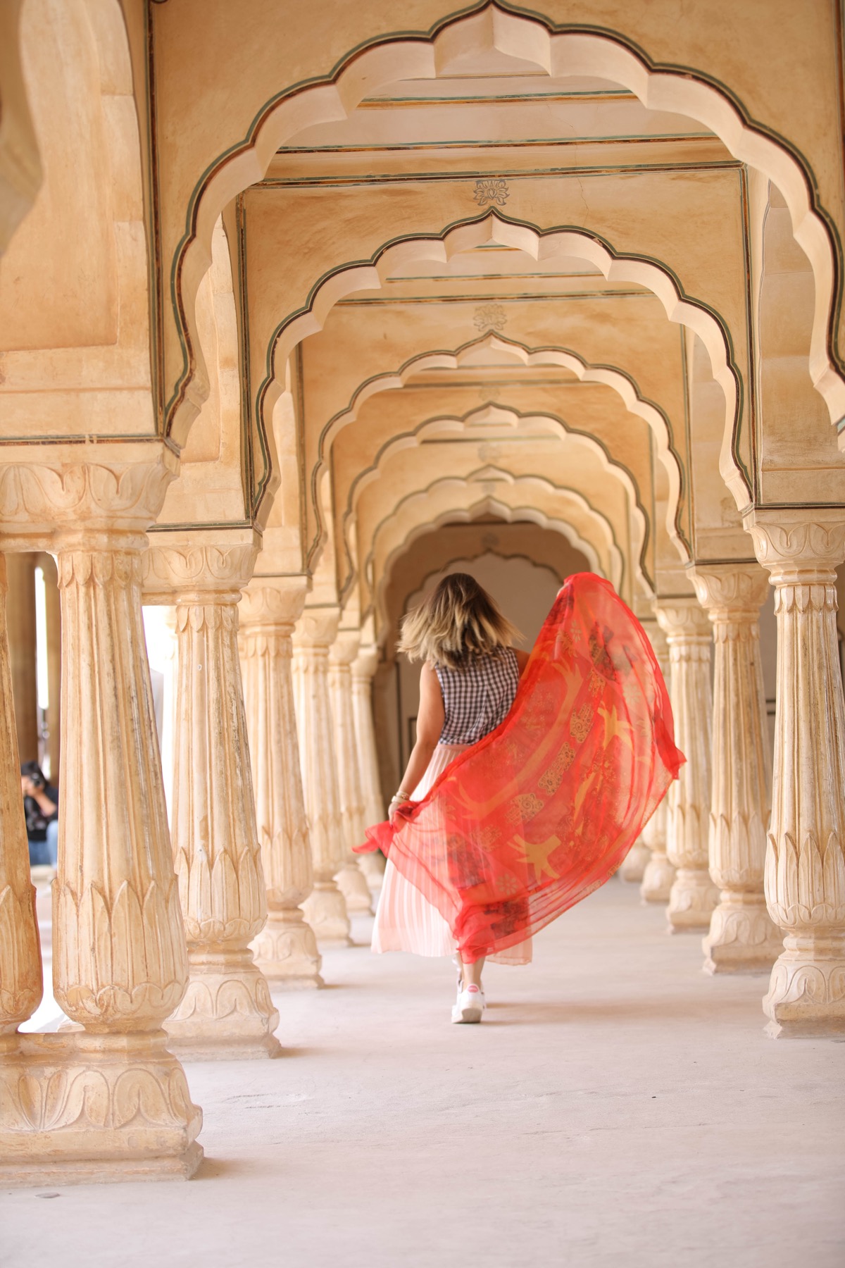 Walking through ornate arches in India with a flowing red scarf
